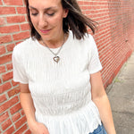 Woman wearing a white blouse and blue jeans against a red brick wall.