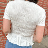Person wearing a white textured top and blue jeans against a brick wall.