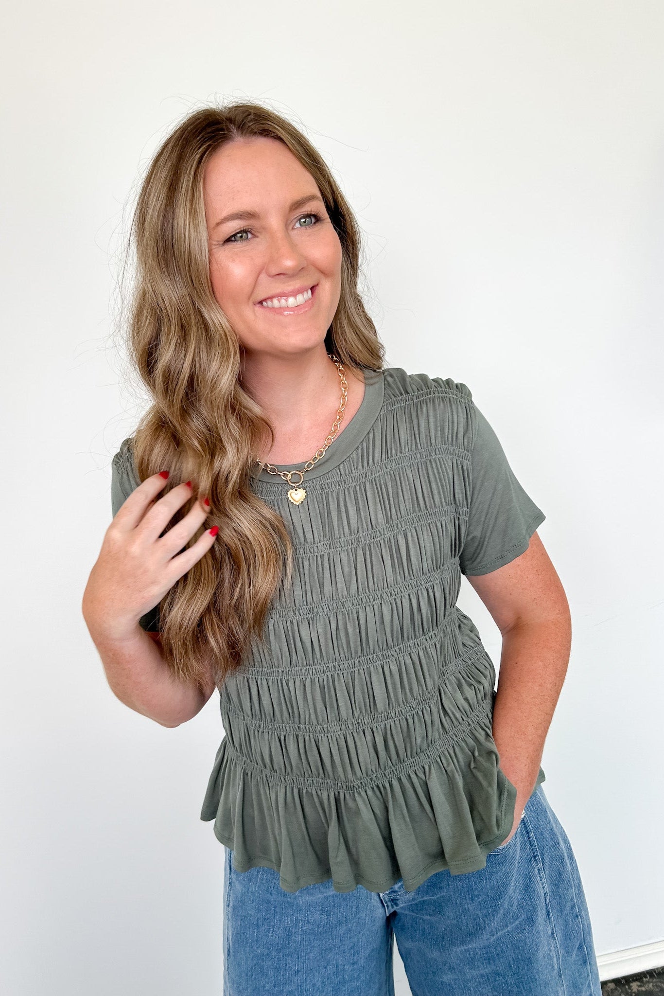 Woman wearing a green ruffled top and blue jeans against a white background