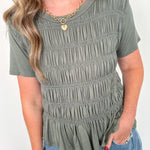 Woman wearing a green smocked top and blue jeans against a white background