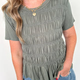 Woman wearing a green smocked top and blue jeans against a white background