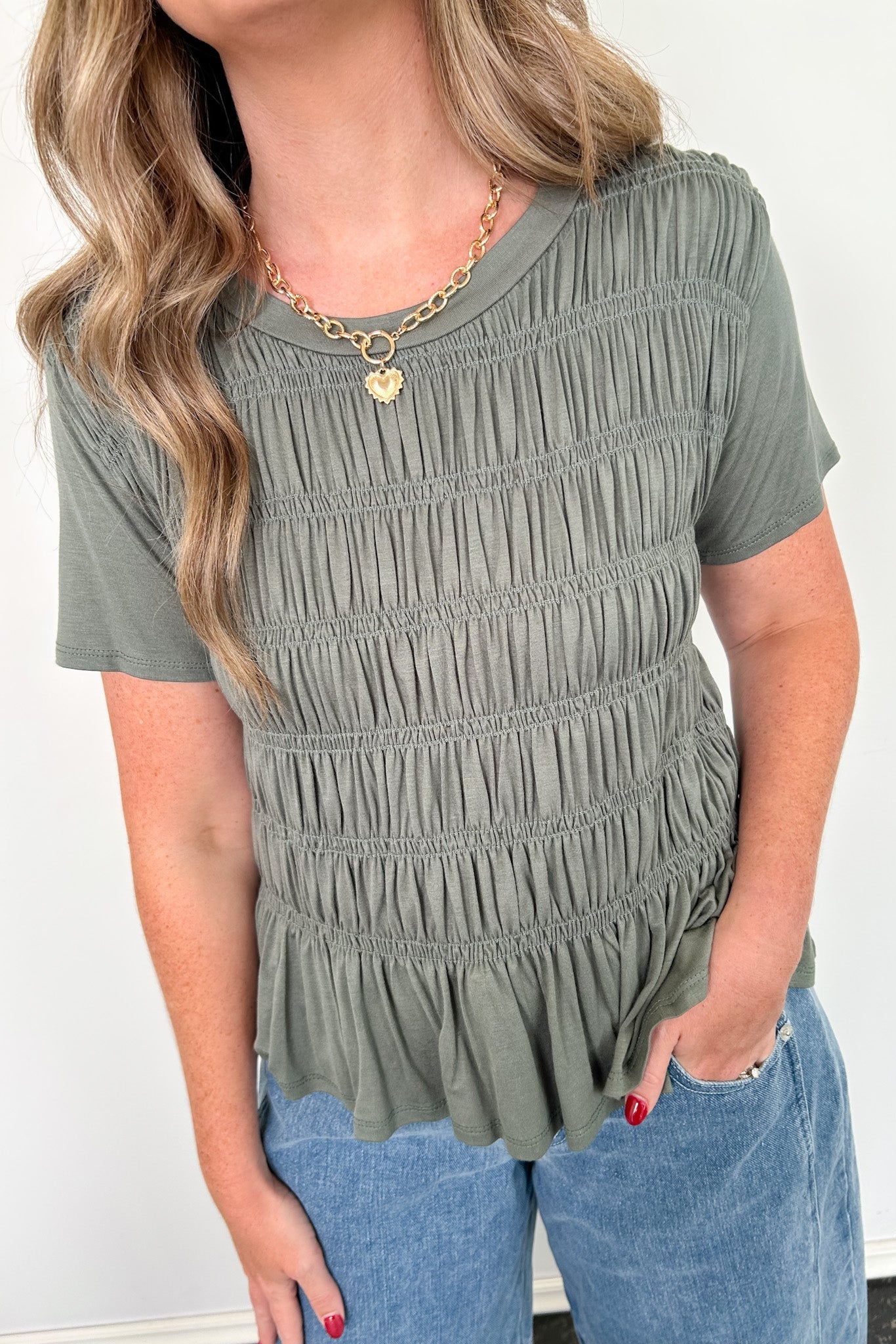 Woman wearing a green smocked top and blue jeans against a white background