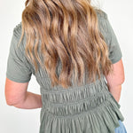 Person wearing a green peplum top and blue jeans with a plain background