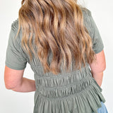 Person wearing a green peplum top and blue jeans with a plain background