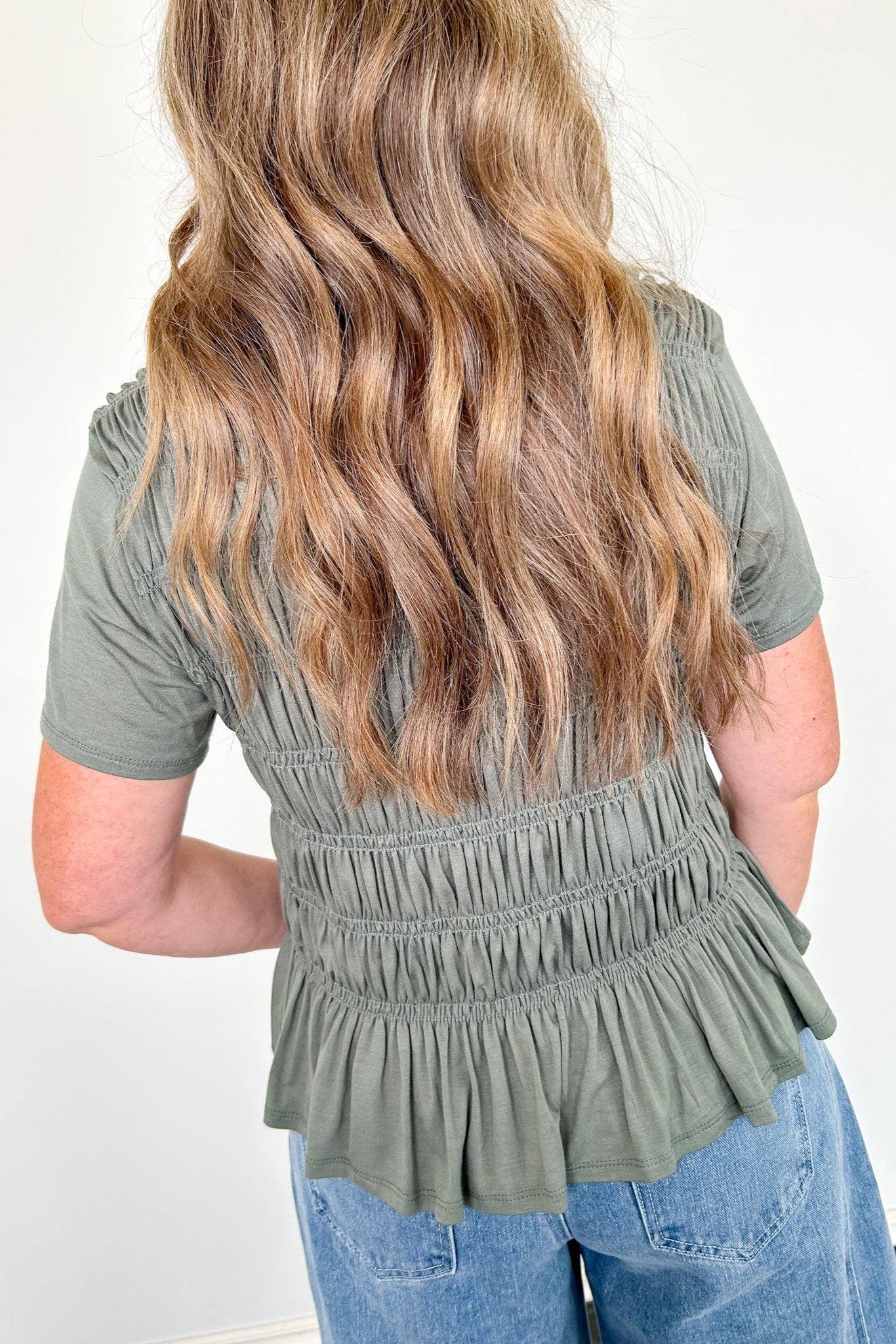 Person wearing a green peplum top and blue jeans with a plain background