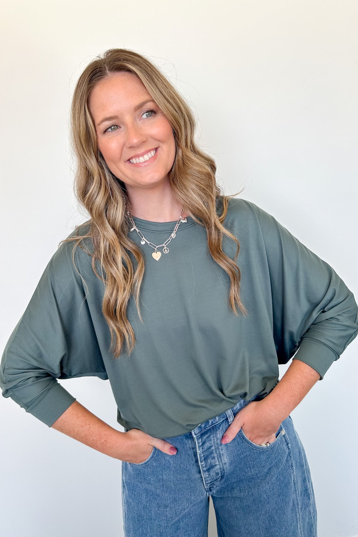 Woman wearing a green sweater and blue jeans against a white background