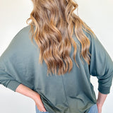 Person wearing a green long-sleeve shirt and blue jeans with a plain background