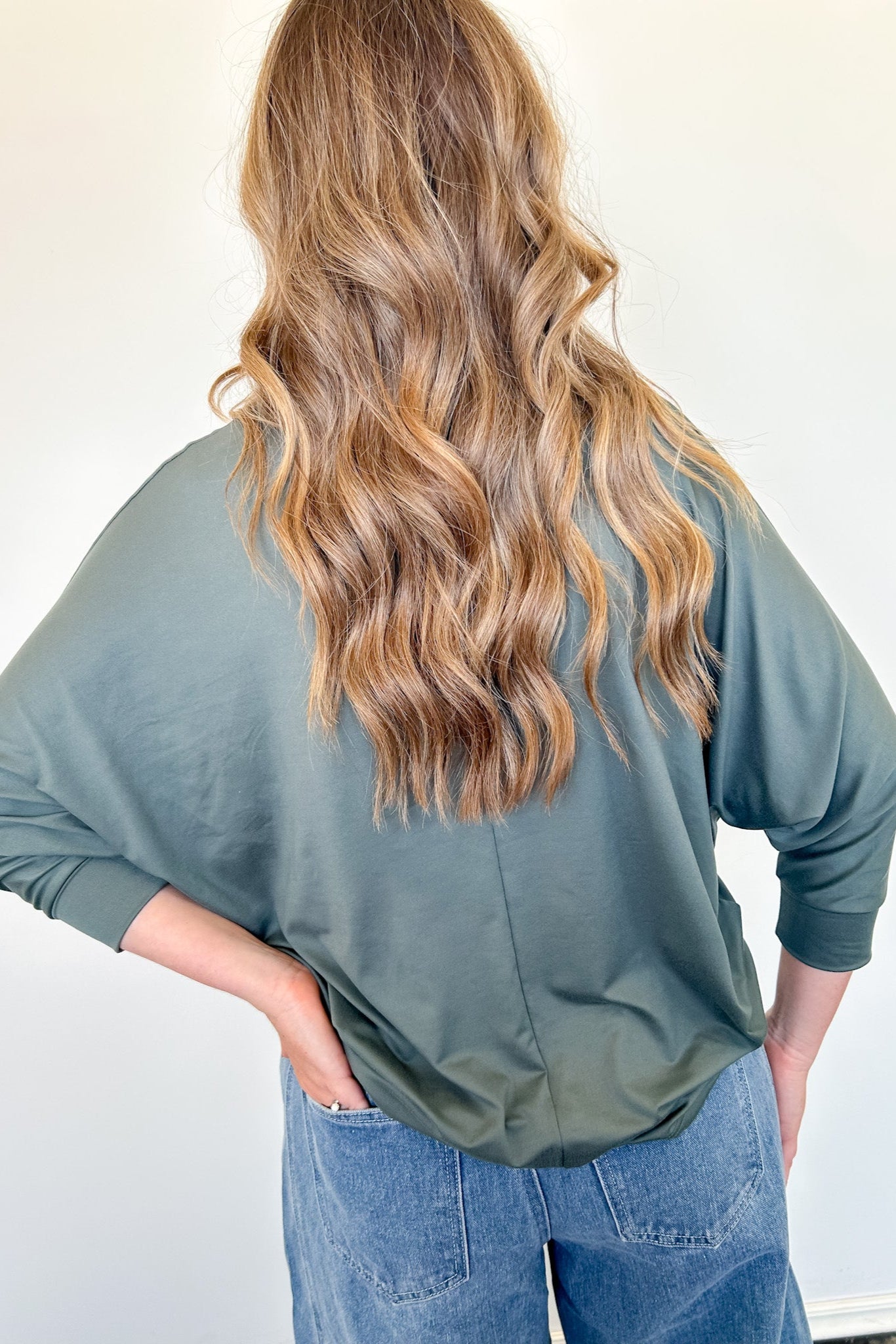 Person wearing a green long-sleeve shirt and blue jeans with a plain background