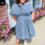 Woman wearing a blue dress standing outside a building with pink flowers.