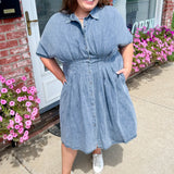 Woman wearing a blue dress standing outside a building with pink flowers.