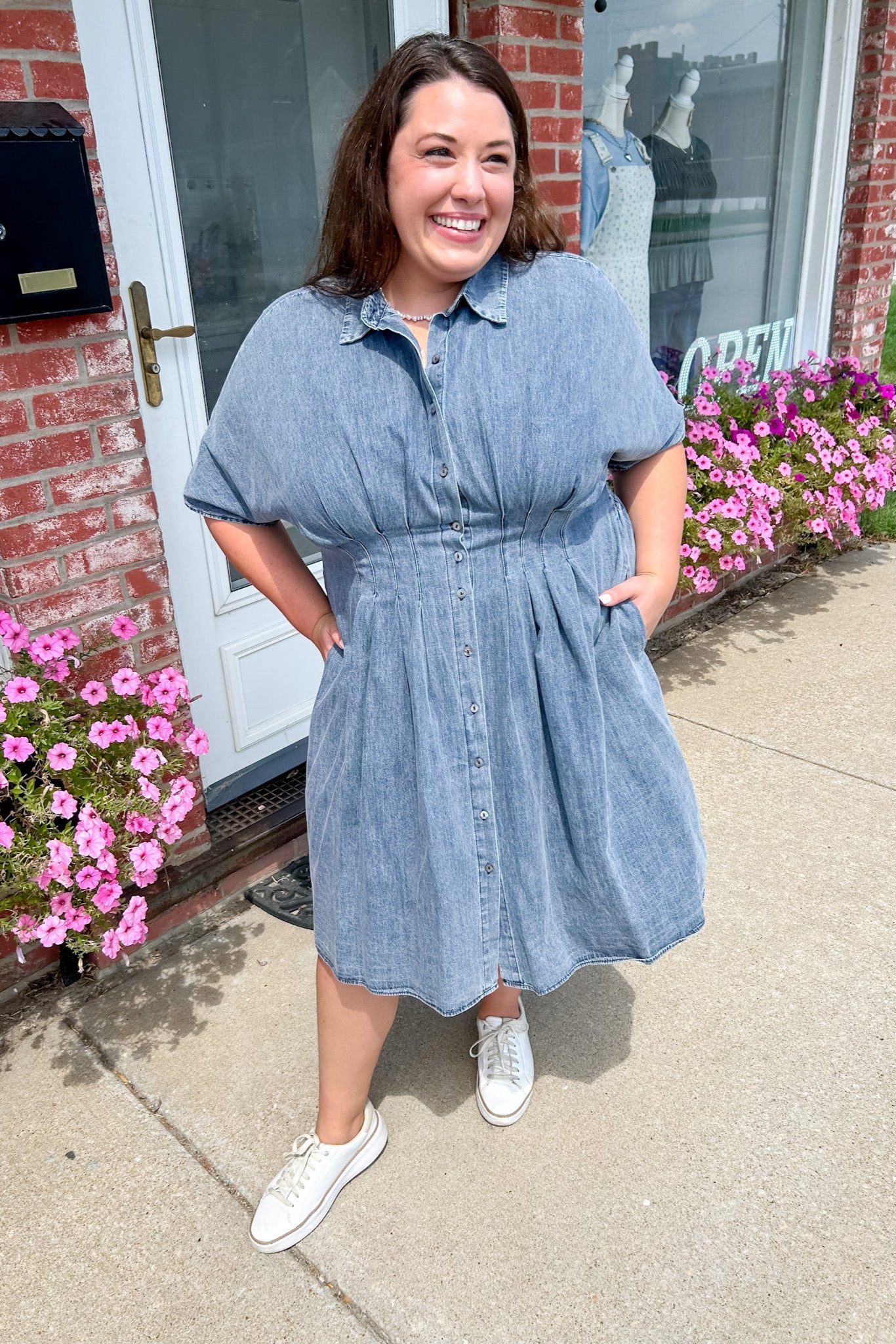 Woman wearing a blue dress standing outside a building with pink flowers.