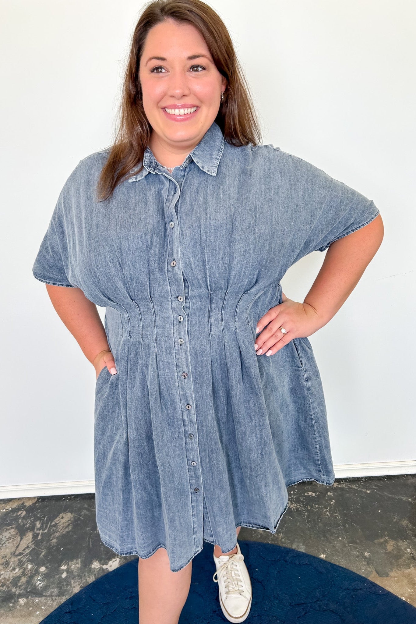 Woman wearing a denim dress standing against a white wall.