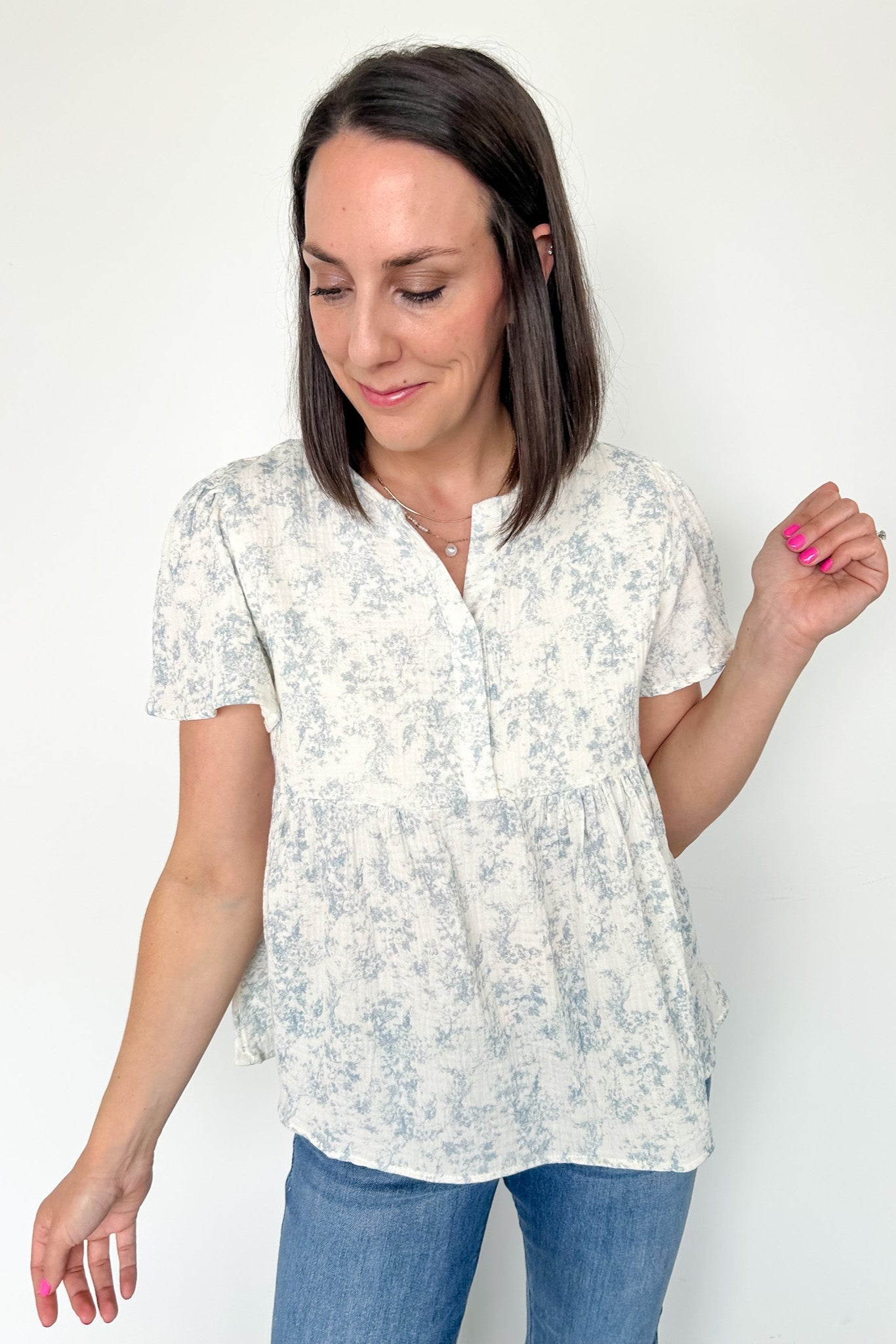 Short flowy sleeved top with button detailing. Cream in color with light blue floral pattern. Babydoll style.