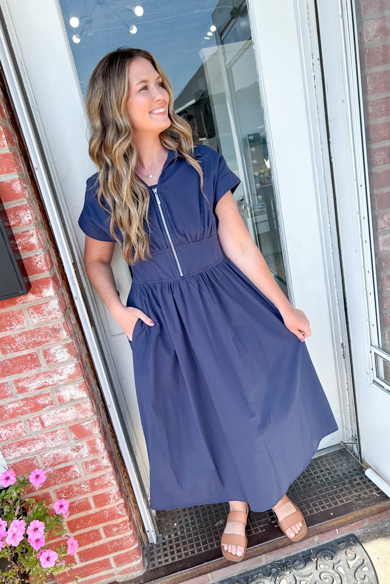 Woman in a blue dress standing outside a building with a brick wall and glass door.