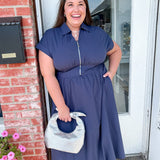 Woman in a blue dress standing outside a building with pink flowers and a mailbox.