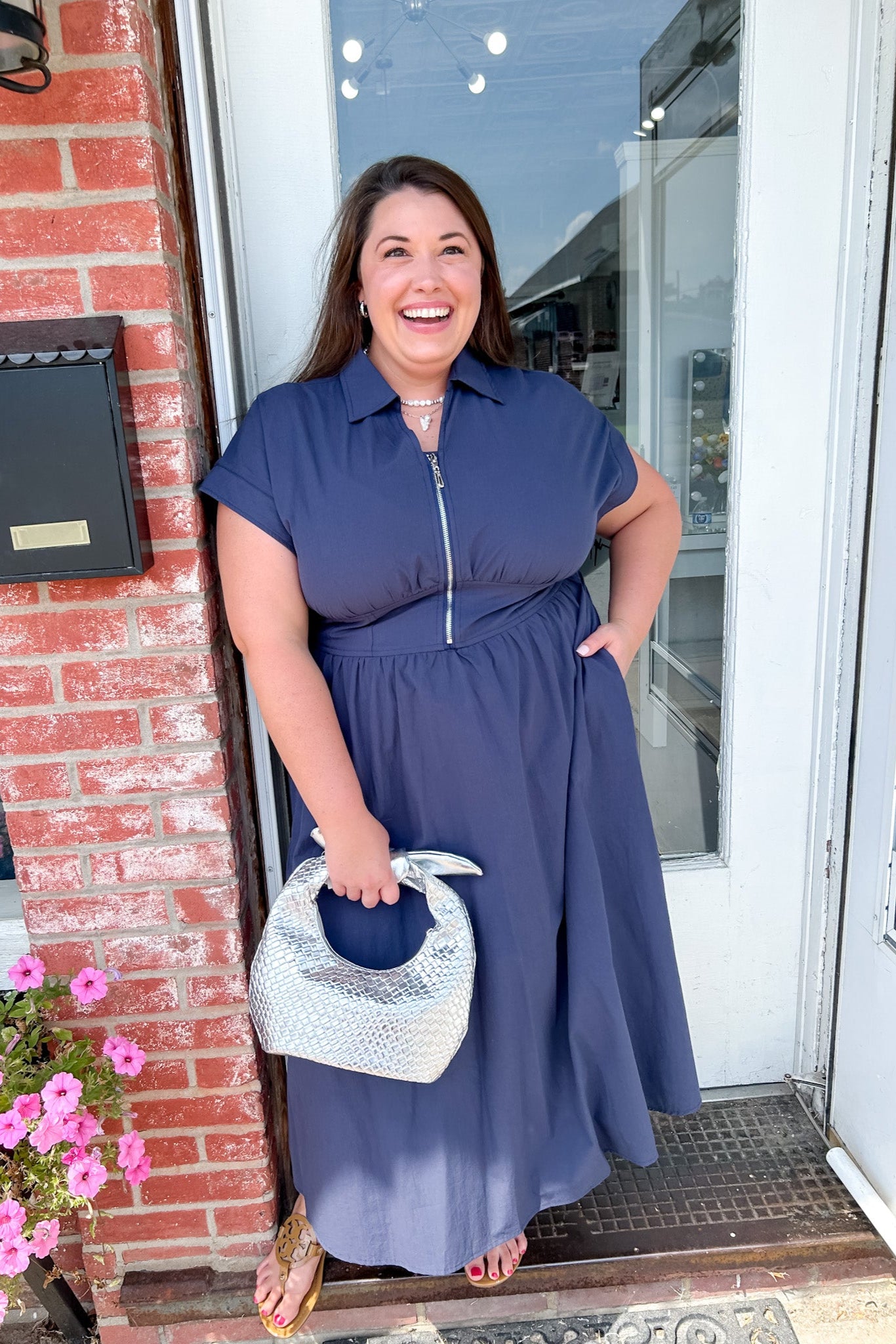 Woman in a blue dress standing outside a building with pink flowers and a mailbox.