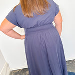 Person wearing a purple dress standing against a white wall.
