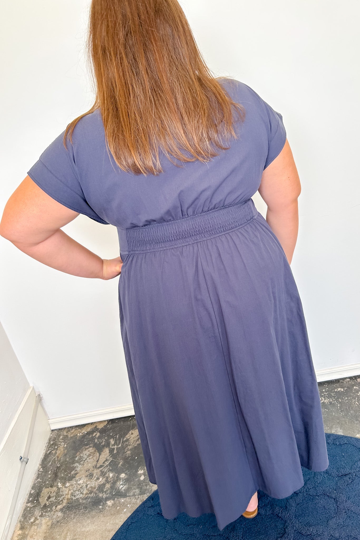 Person wearing a purple dress standing against a white wall.