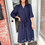 Woman in a navy dress standing outside a building with brick walls.