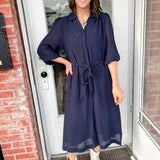 Woman in a navy dress standing outside a building with brick walls.