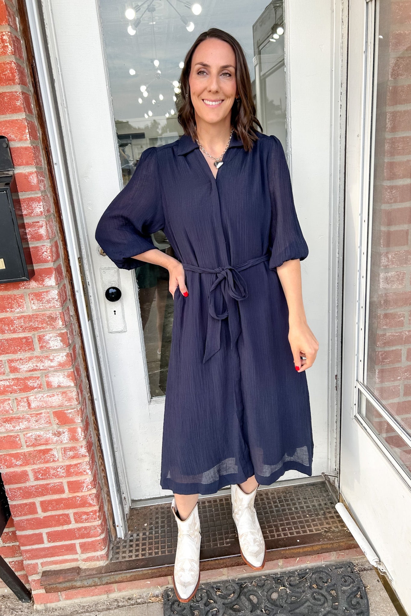 Woman in a navy dress standing outside a building with brick walls.