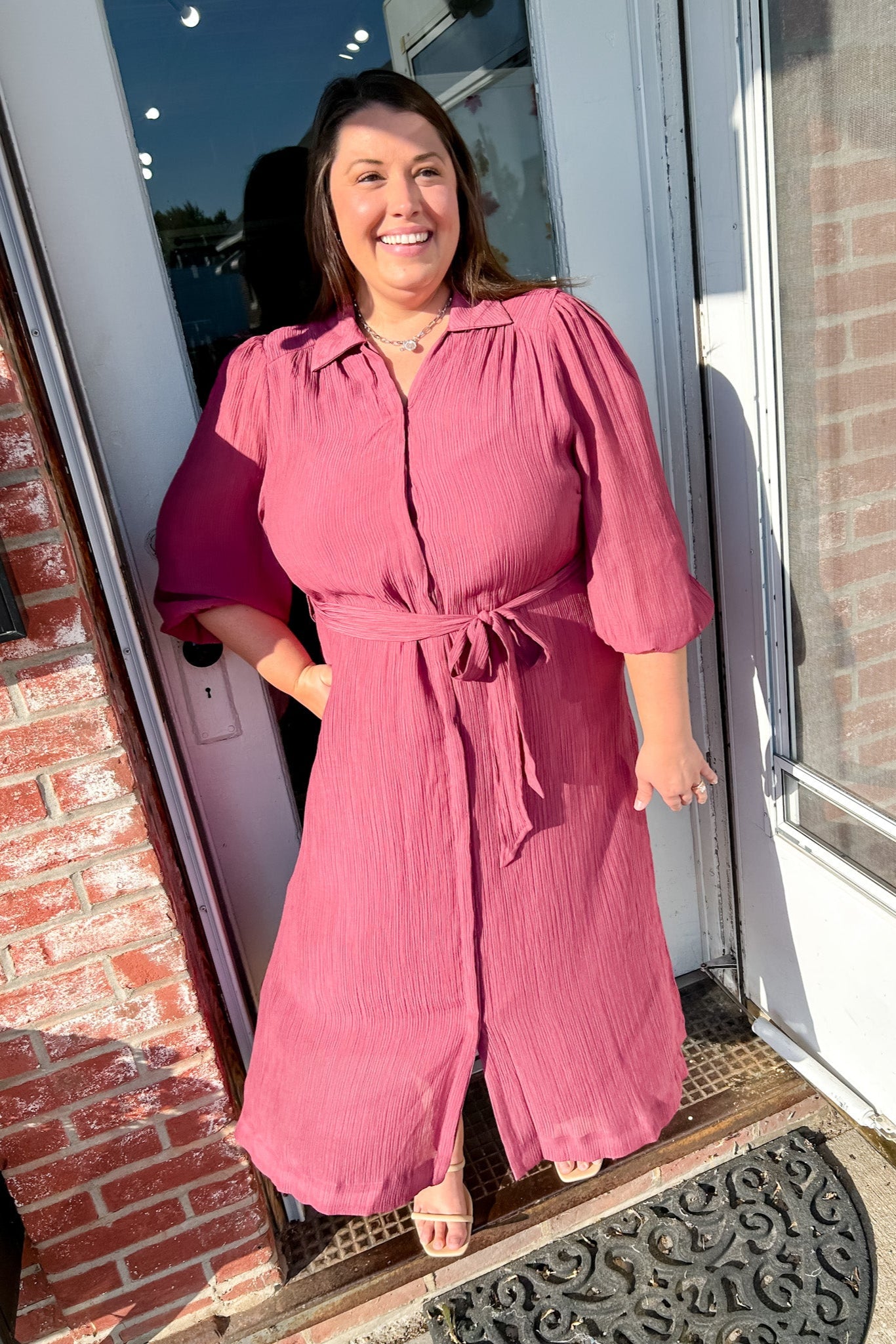 Woman in a pink dress standing in front of a door with a brick wall background