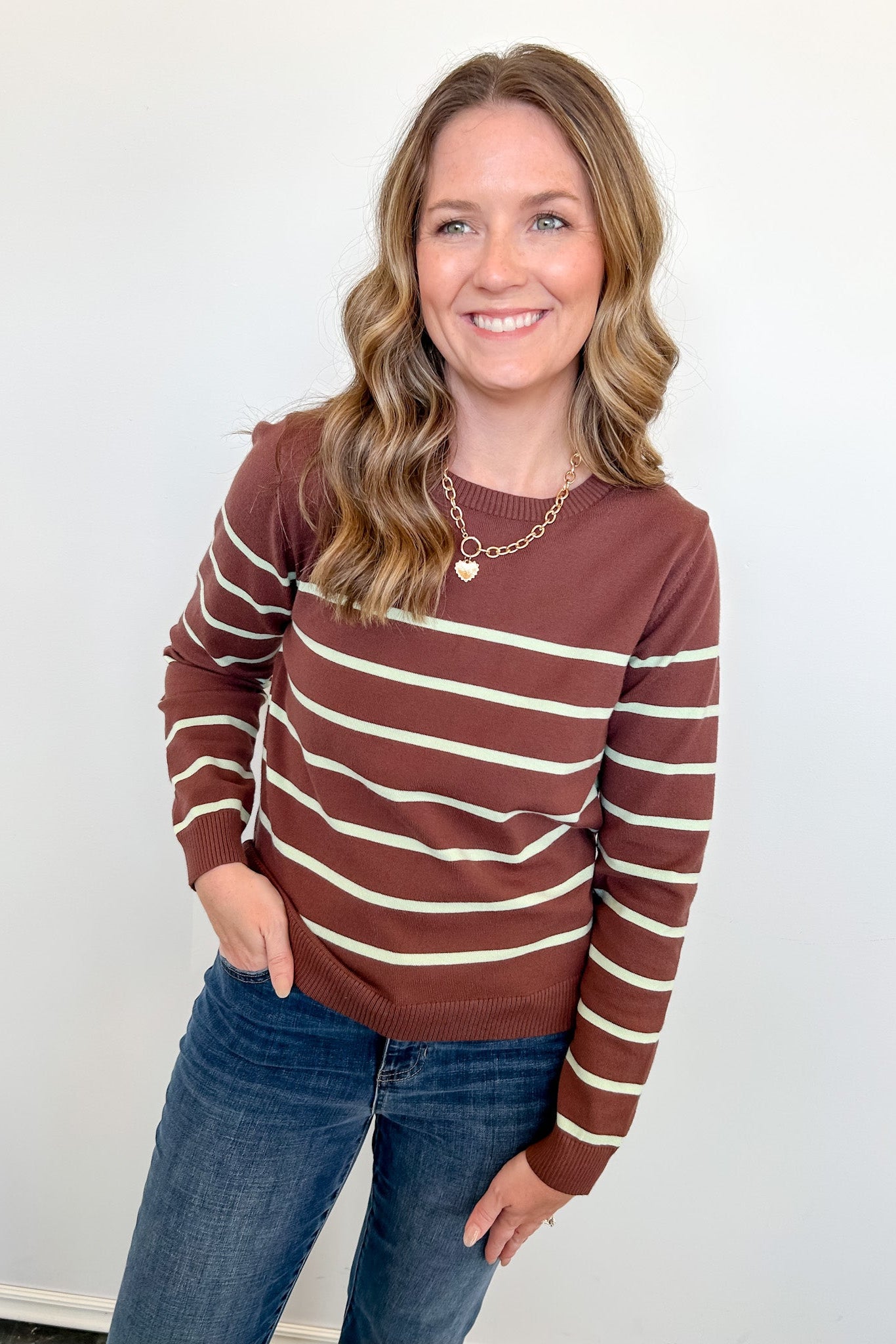 Woman wearing a brown and beige striped sweater and blue jeans against a white background