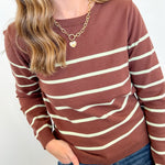 Person wearing a brown and beige striped sweater with blue jeans on a white background