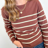Person wearing a brown and beige striped sweater with blue jeans on a white background