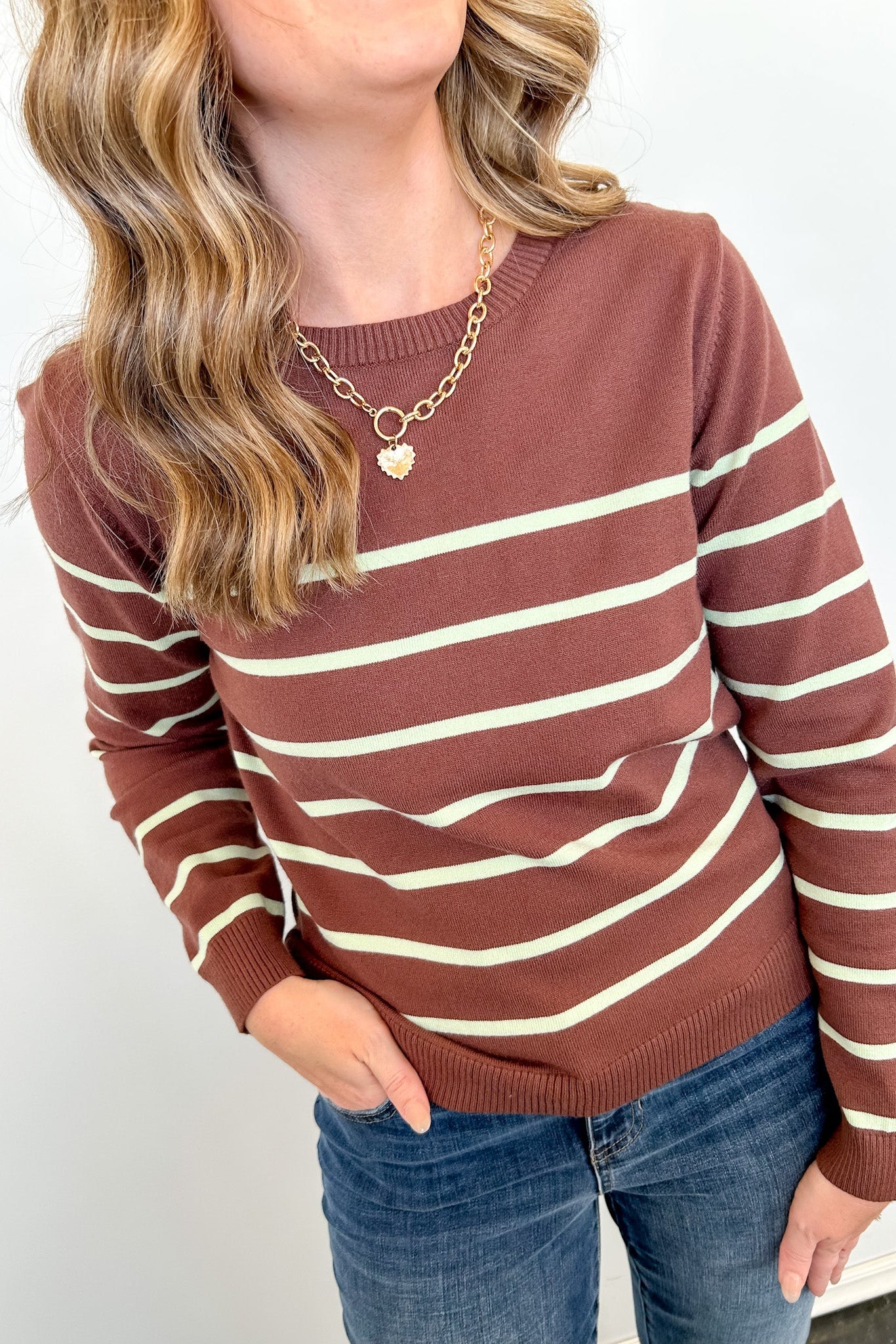 Person wearing a brown and beige striped sweater with blue jeans on a white background