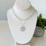 Necklace on a white bust with a plant in the background