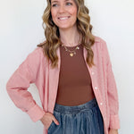 Woman wearing a pink striped shirt, brown top, and blue jeans against a white background