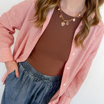 Woman wearing a pink striped shirt over a brown top and blue jeans against a white background