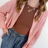 Woman wearing a pink striped shirt over a brown top and blue jeans against a white background