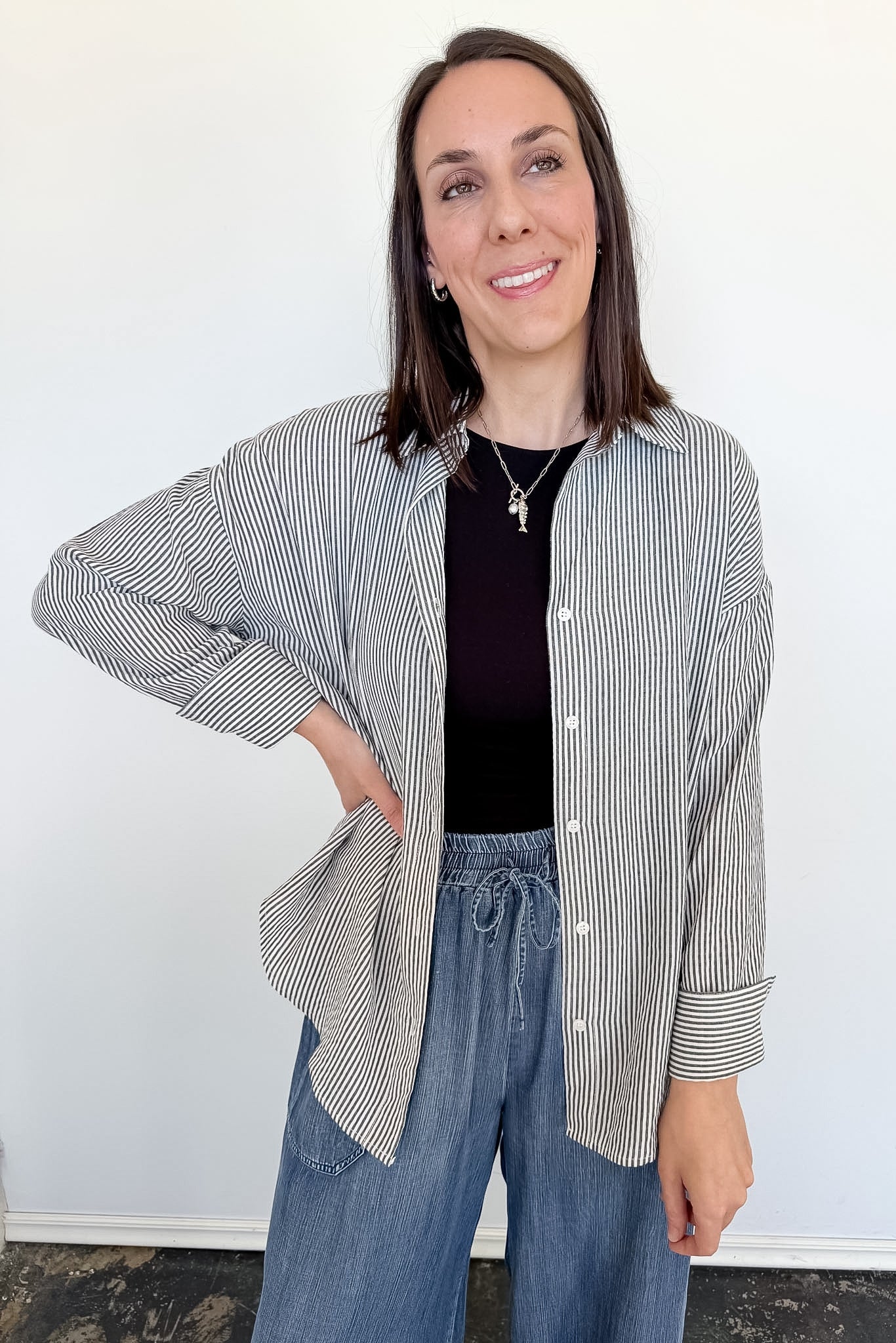Woman wearing a striped shirt and blue jeans against a white wall