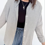 Woman wearing a striped shirt, black top, and blue jeans against a white background