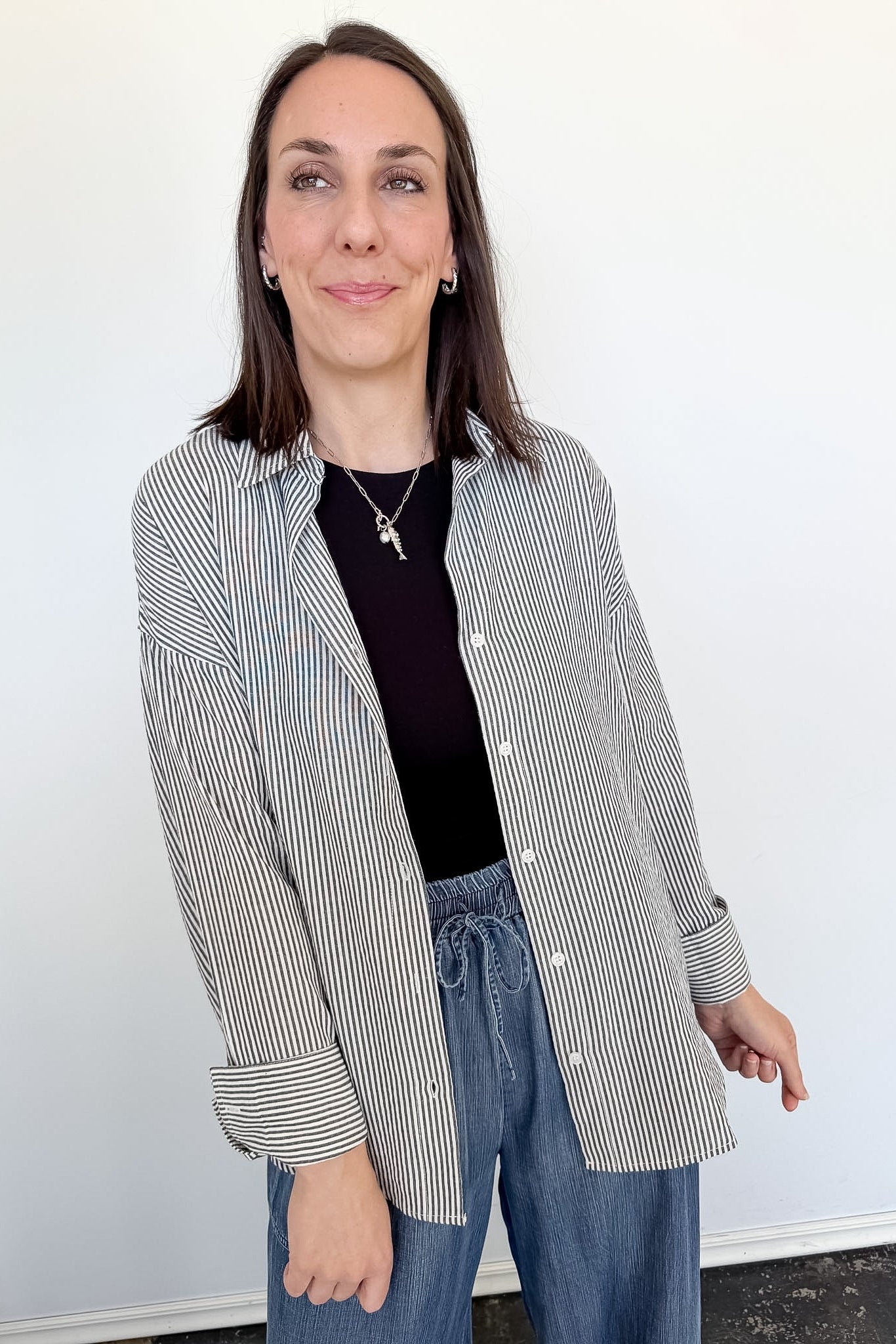 Woman wearing a striped shirt and blue jeans against a white wall