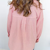 Person wearing a pink and white striped shirt with long hair, standing against a white wall.