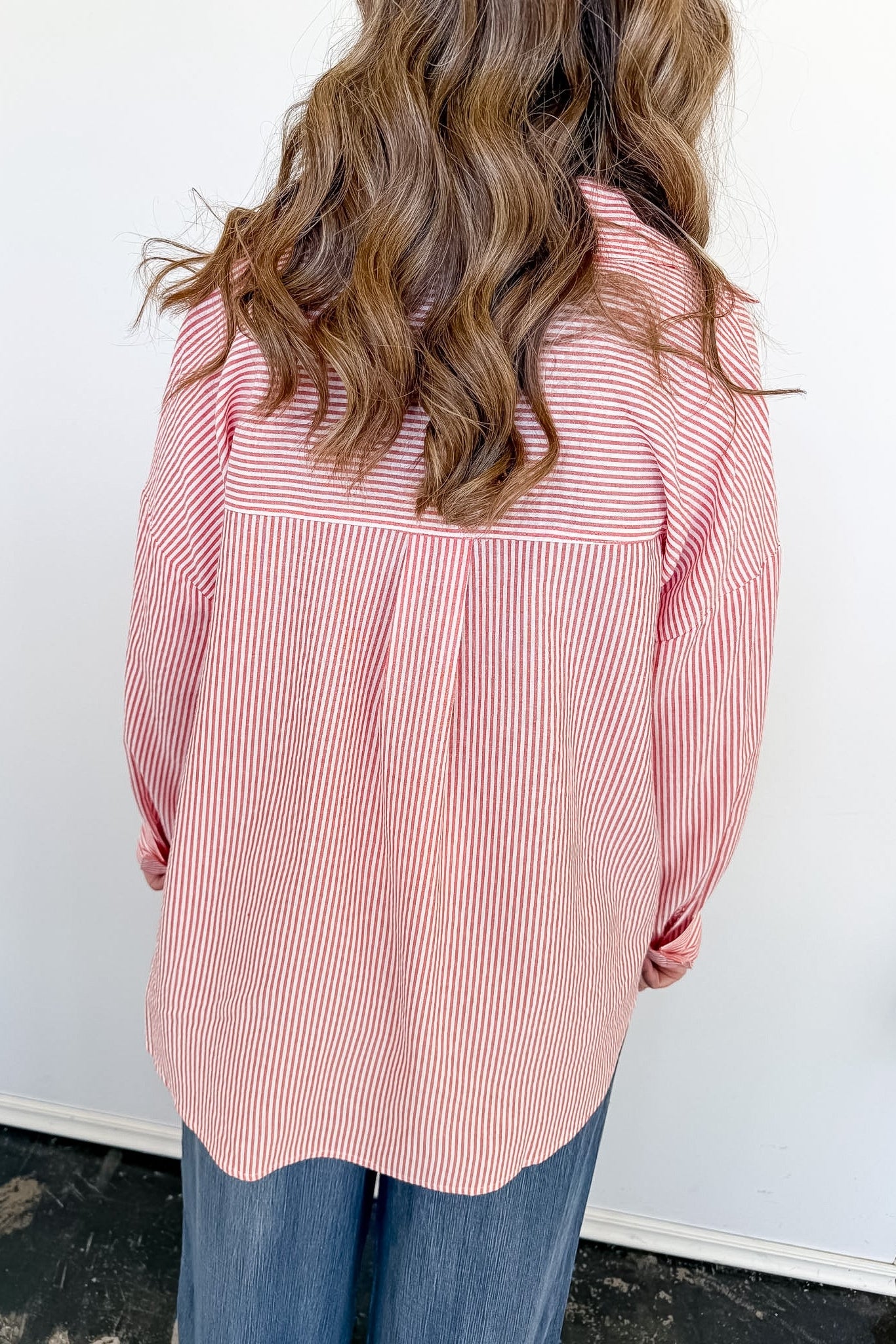 Person wearing a pink and white striped shirt with long hair, standing against a white wall.