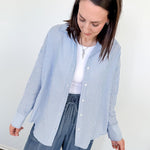 Woman wearing a blue and white striped shirt and blue pants against a white wall.