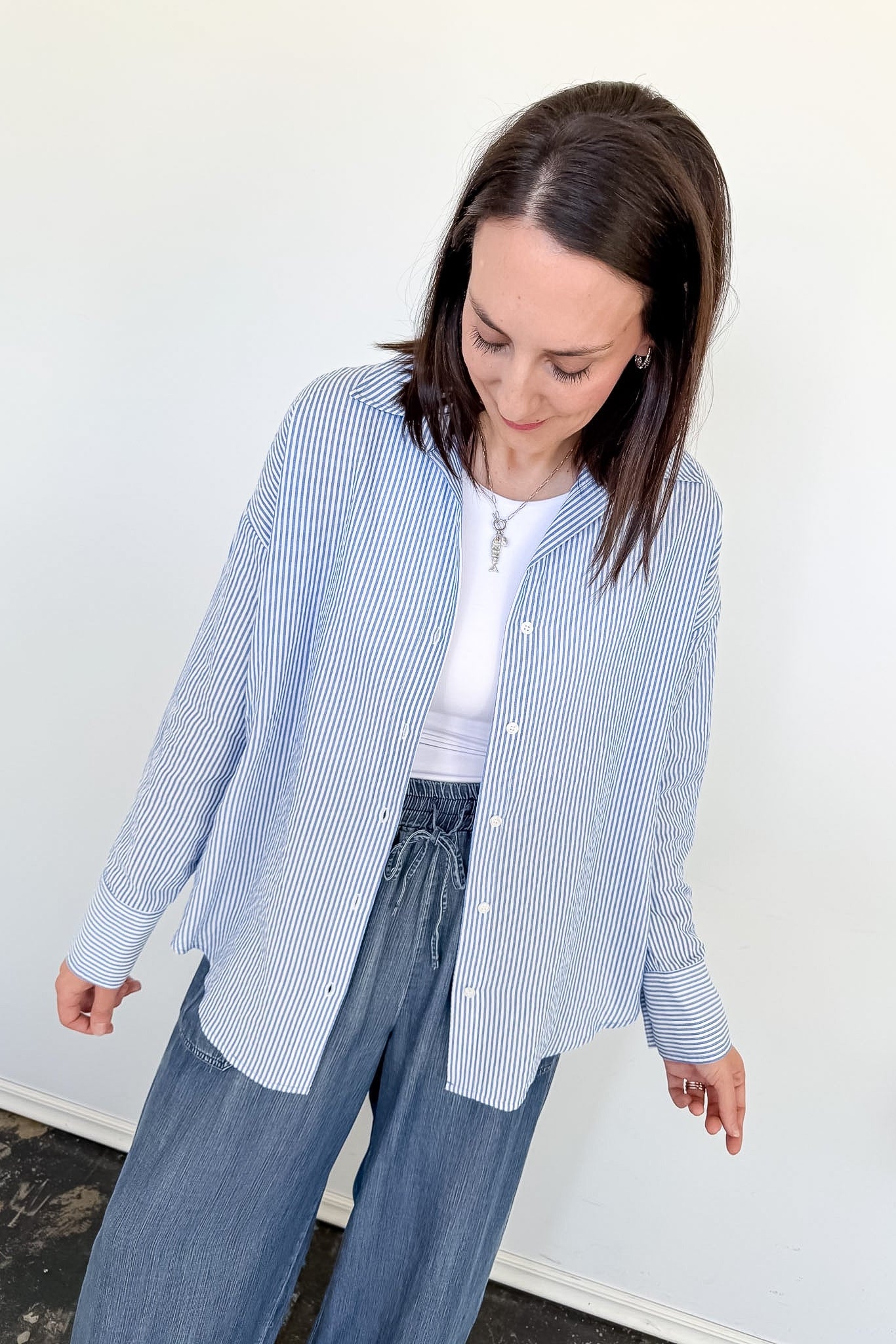 Woman wearing a blue and white striped shirt and blue pants against a white wall.