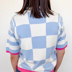 Person wearing a checkered shirt with blue, white, and pink colors against a plain background