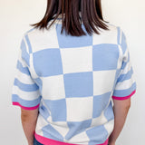 Person wearing a checkered shirt with blue, white, and pink colors against a plain background