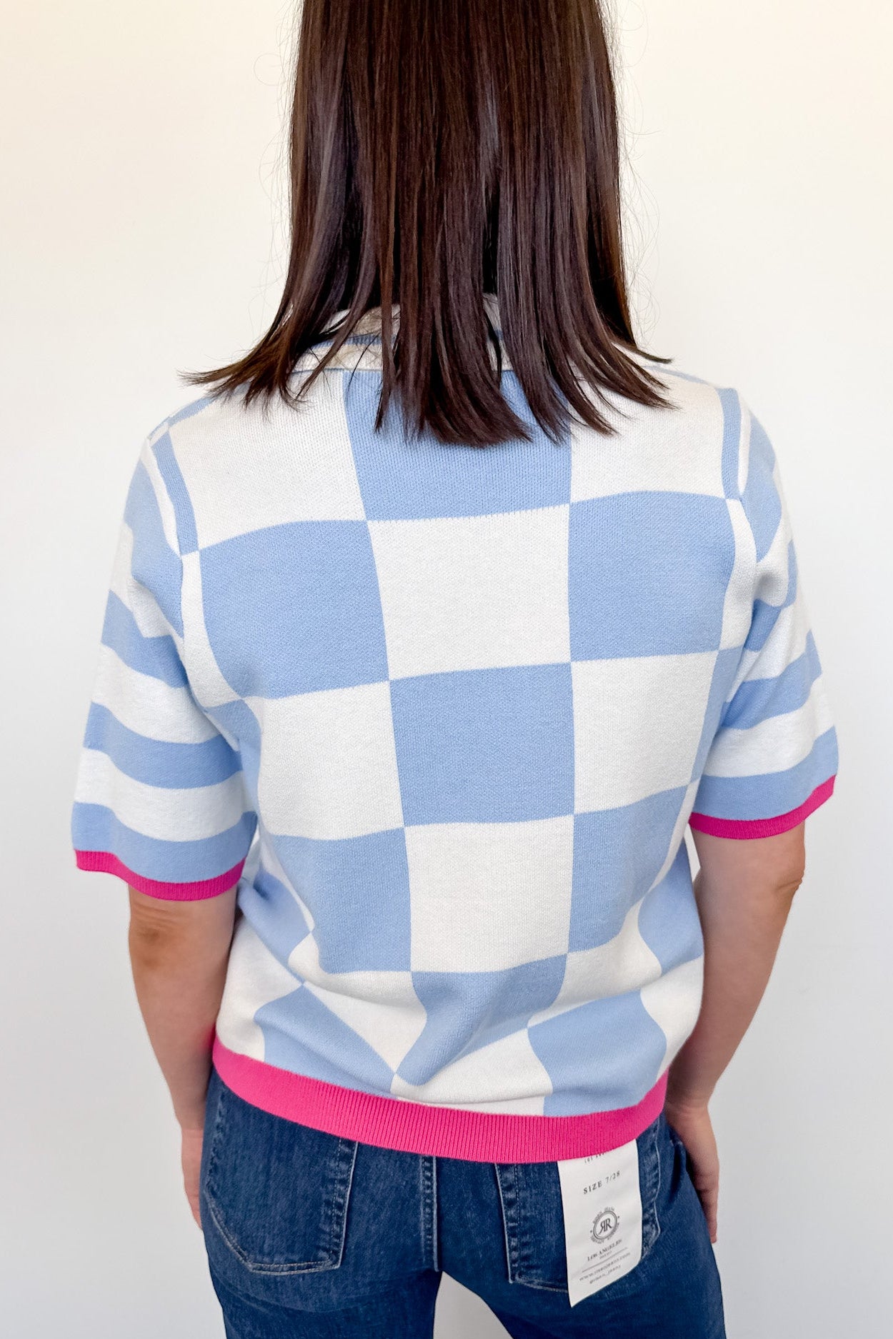 Person wearing a checkered shirt with blue, white, and pink colors against a plain background