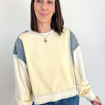 Woman wearing a cream and blue color-blocked sweatshirt against a white background
