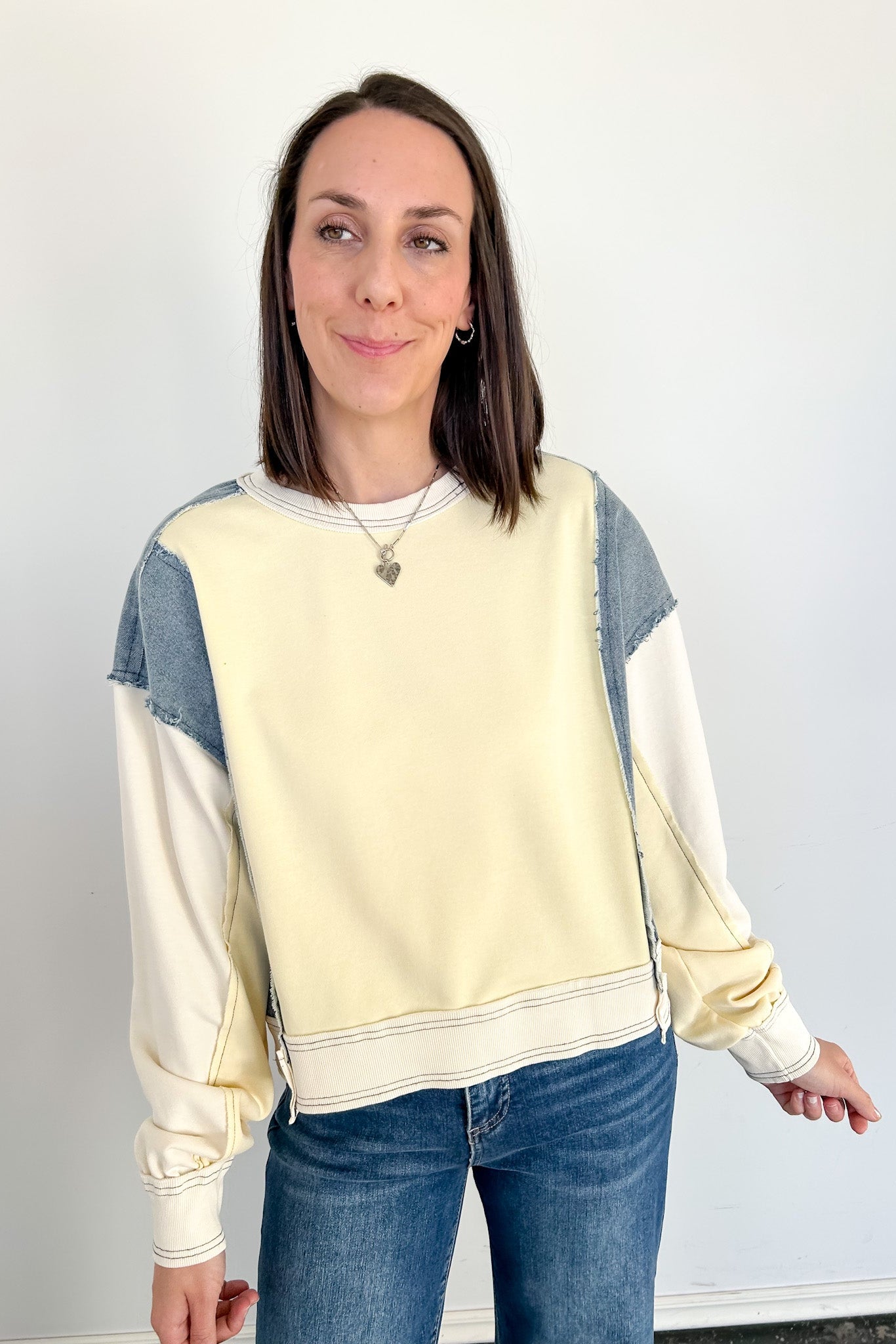 Woman wearing a cream and blue color-blocked sweatshirt against a white background