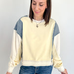 Woman wearing a cream and blue color-blocked sweatshirt against a white background
