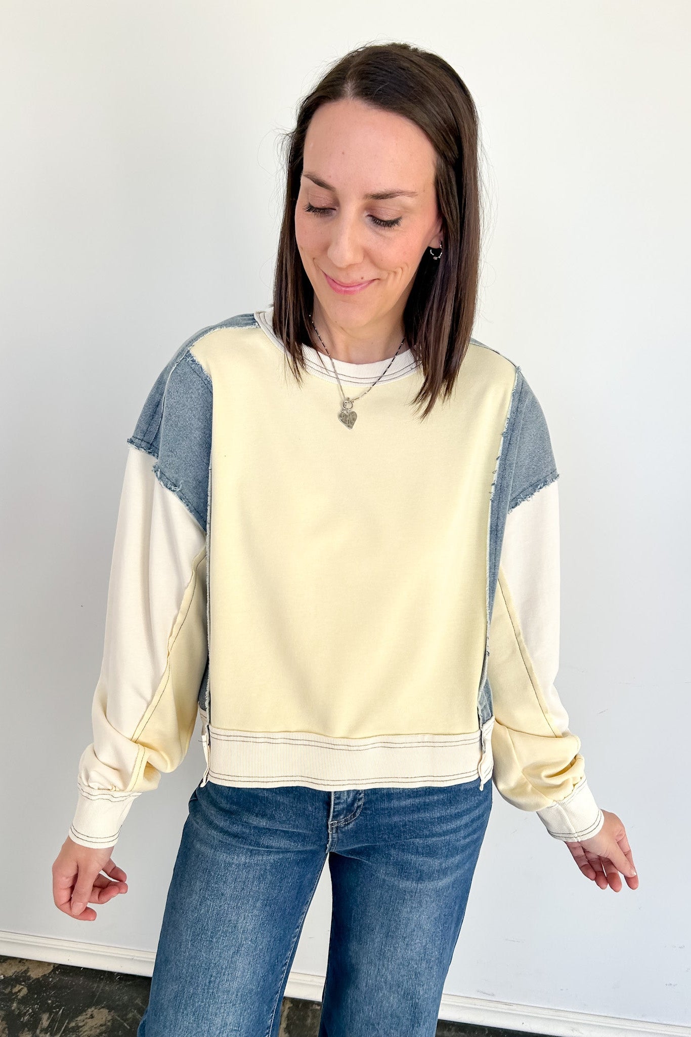 Woman wearing a cream and blue color-blocked sweatshirt against a white background