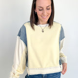 Woman wearing a cream and blue color-blocked sweatshirt against a white background