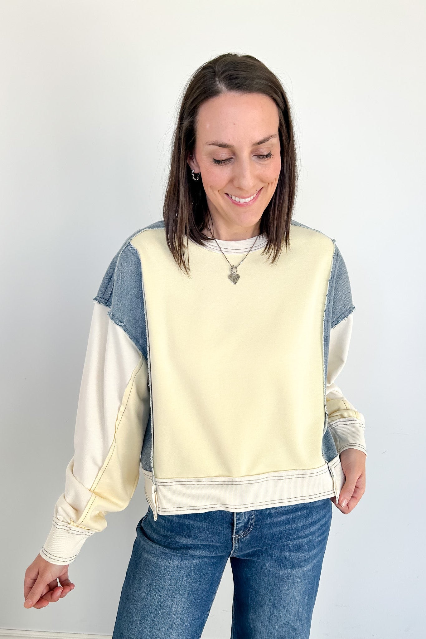 Woman wearing a cream and blue color-blocked sweatshirt against a white background